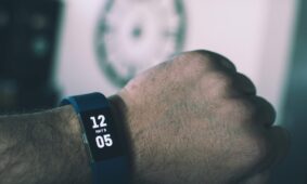 Close-up of a digital smartwatch showing time and date on a man's wrist indoors.