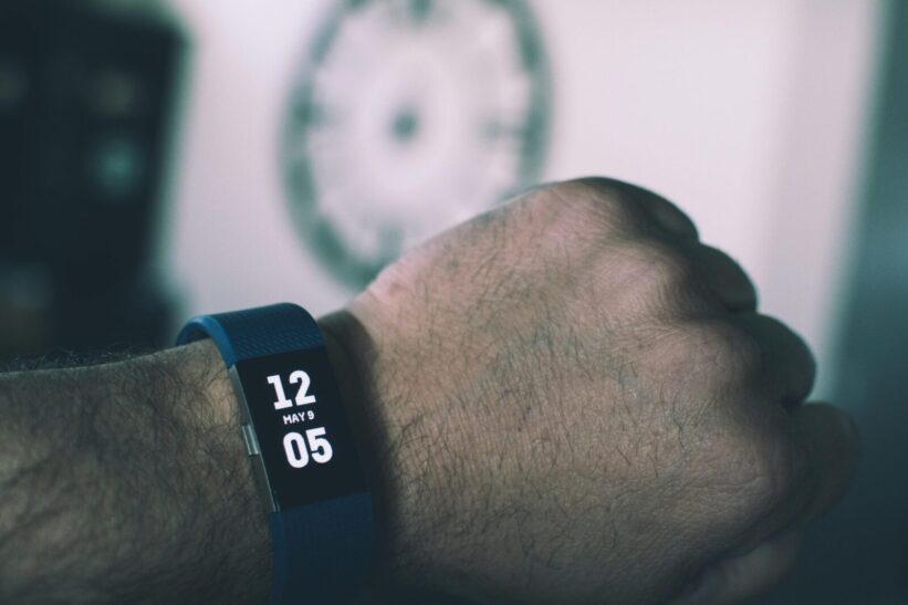 Close-up of a digital smartwatch showing time and date on a man's wrist indoors.