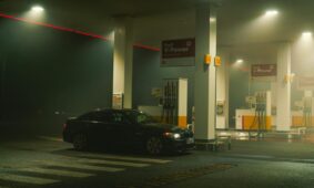 A BMW sports car parked at a Shell gas station at night, featuring bright lights and an urban setting.