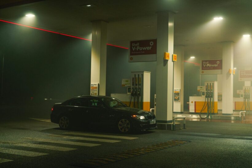 A BMW sports car parked at a Shell gas station at night, featuring bright lights and an urban setting.