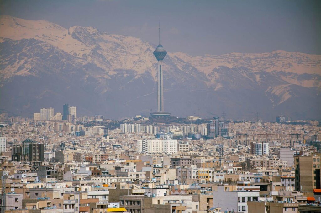 Aerial view of Tehran featuring Milad Tower against the Alborz Mountains.