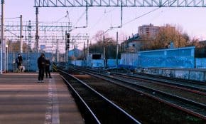 A calm train station scene with people waiting on the platform during the day.