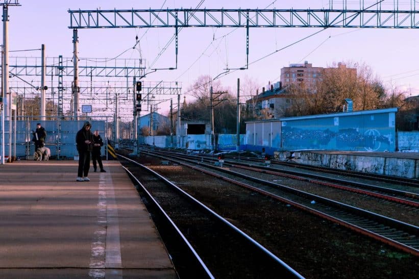 A calm train station scene with people waiting on the platform during the day.