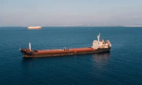 Aerial view of a cargo ship sailing in the open sea under clear skies, showcasing maritime transport.
