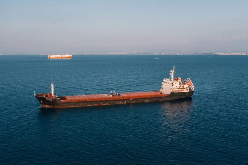 Aerial view of a cargo ship sailing in the open sea under clear skies, showcasing maritime transport.