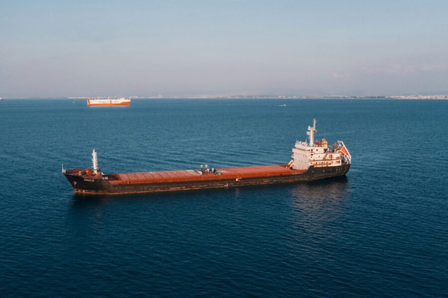 Aerial view of a cargo ship sailing in the open sea under clear skies, showcasing maritime transport.