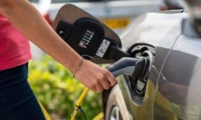 Close-up of a person plugging in an electric car at a charging station outdoors.
