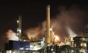 A nighttime view of an industrial factory with smokestacks emitting smoke, highlighting energy production and pollution.