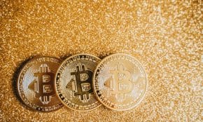 Close-up of three shiny Bitcoin coins on a sparkling gold glitter background, symbolizing cryptocurrency wealth.