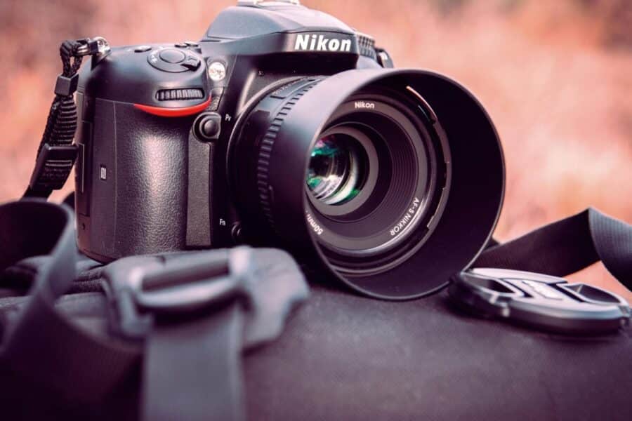 Nikon DSLR camera with lens cap on backpack, showcasing photography gear in an outdoor setting.