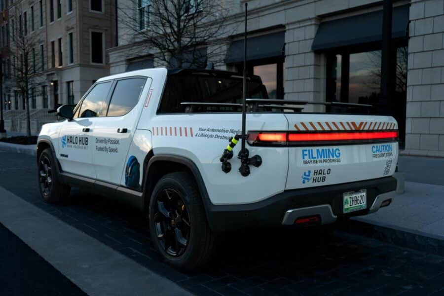 A white truck equipped for filming parked on a city street during twilight.