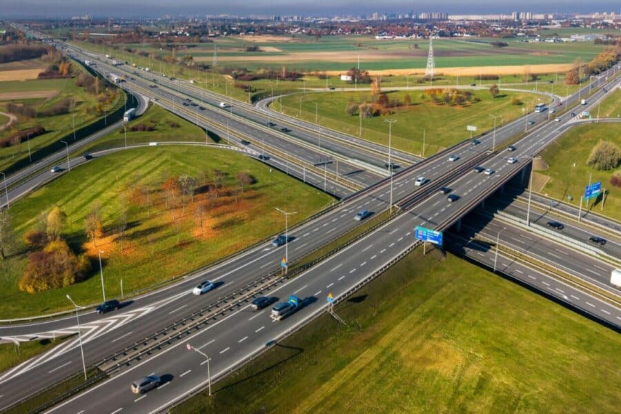 Aerial shot capturing a highway intersection in Poznań, Poland with fall foliage and light urban traffic.
