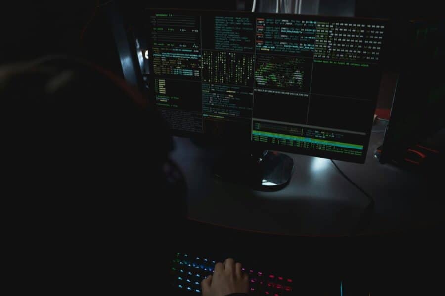 Dark room setup with code displayed on PC monitors highlighting cybersecurity themes.