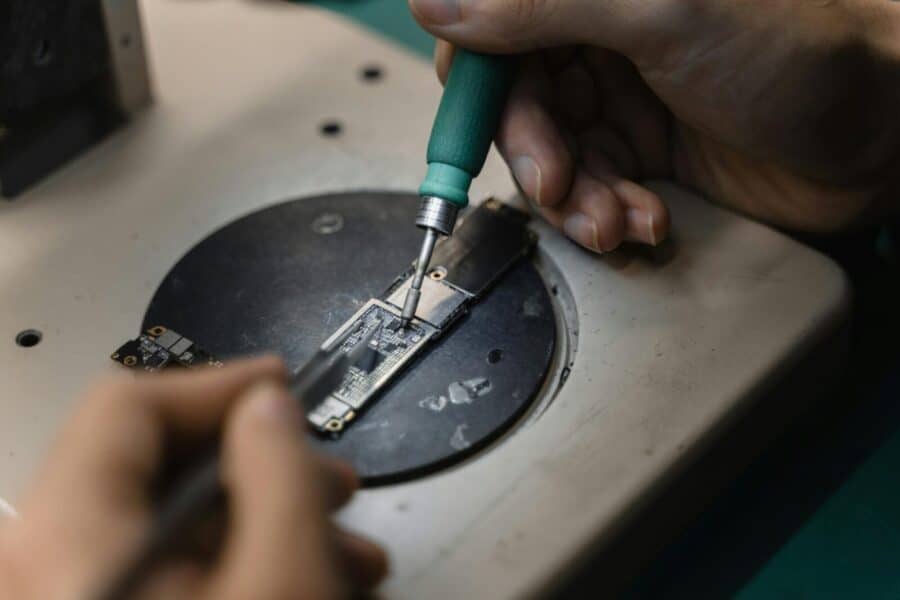 Hands using a soldering iron on circuit board, showcasing precise electronic repair indoors.